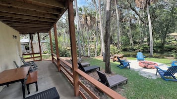 A covered outdoor area with wooden furniture, a fire pit, and a pond.