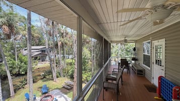 Un portico riparato con vista su un giardino, un tavolo con sedie e una porta.