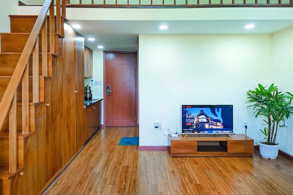Ein modernes Wohnzimmer mit einer Holztreppe, einem Flachbildfernseher auf einem Holzboden und einer Topfpflanze.