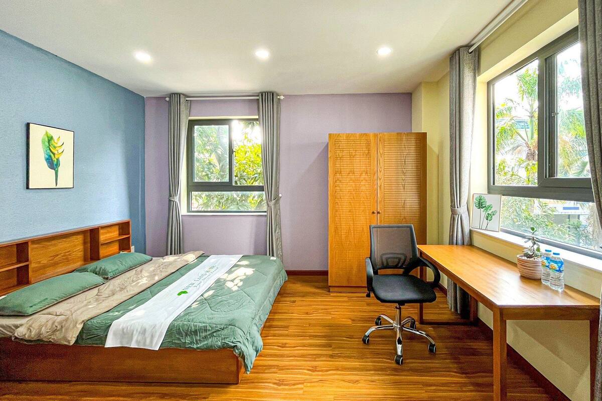 Ein Schlafzimmer mit Bett, Schreibtisch, Stuhl, Kleiderschrank und Fenstern mit Vorhängen.