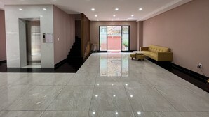 A spacious lobby with a marble floor, a yellow sofa, and a staircase leading to an upper level. - NEW LAND Apartment - Nam Thong 3  (Ho Chi Minh City)