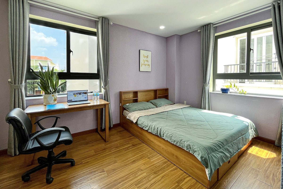 Ein Schlafzimmer mit einem hölzernen Bett, einem Schreibtisch mit einem Laptop, einem Stuhl und einem Fenster mit Vorhängen.