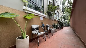 A corridor with potted plants, wicker chairs, and a tiled floor. - NEW LAND Apartment - Nam Thong 3  (Ho Chi Minh City)