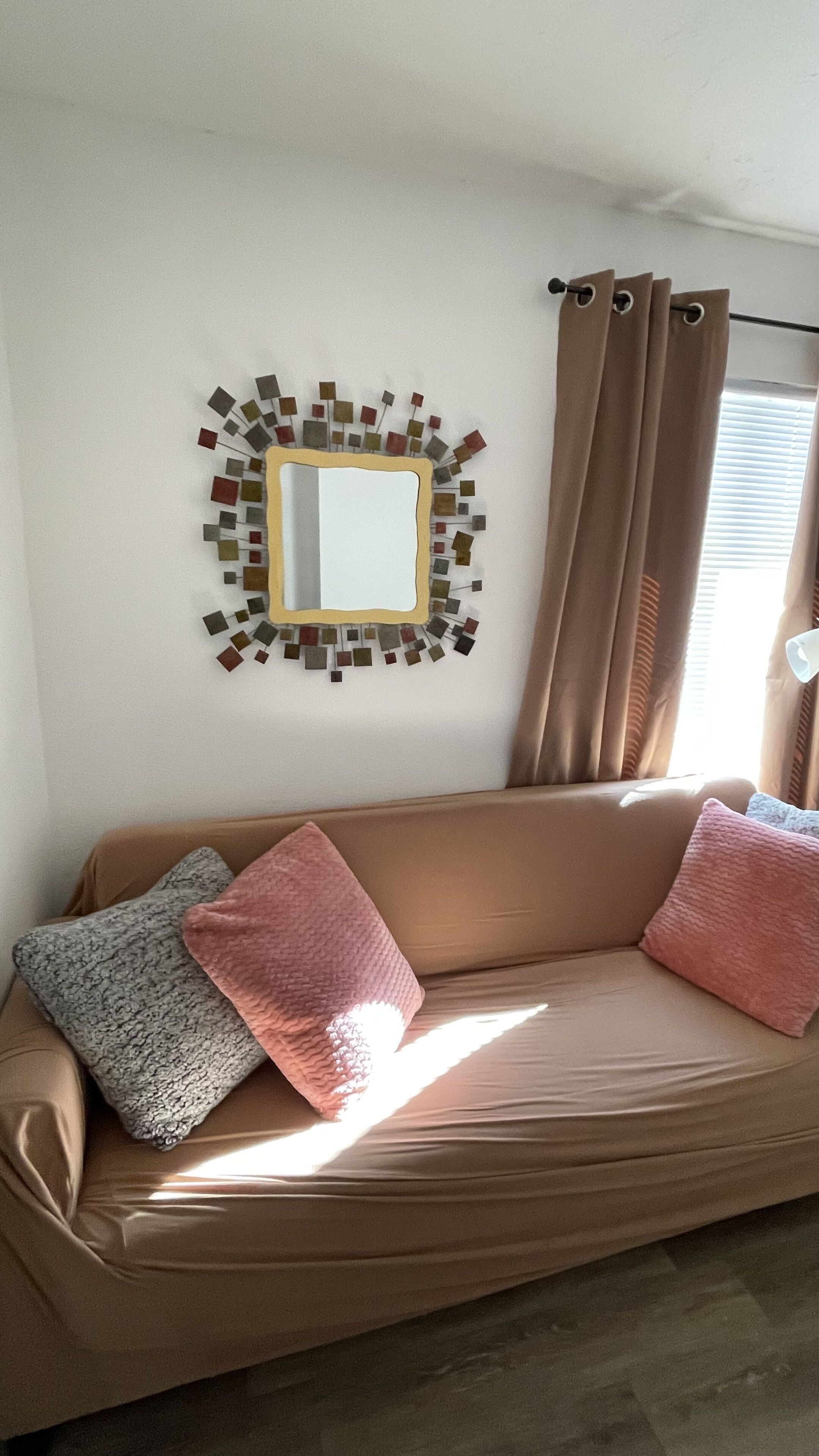 Ein beiges Sofa mit zwei Kissen, einem Wandspiegel und einem dekorativen Mosaik.