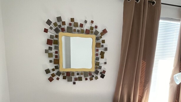 A beige sofa with two pillows, a wall-mounted mirror, and a decorative mosaic. - Perfect Desert Getaway  (Borrego Springs)