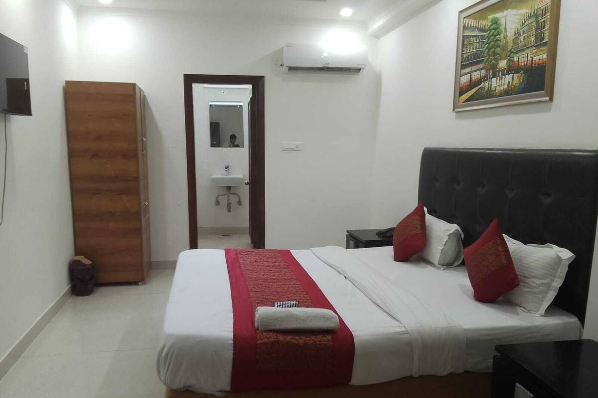 A neatly made bed with a red and white bedspread, a black headboard, and a painting on the wall.
