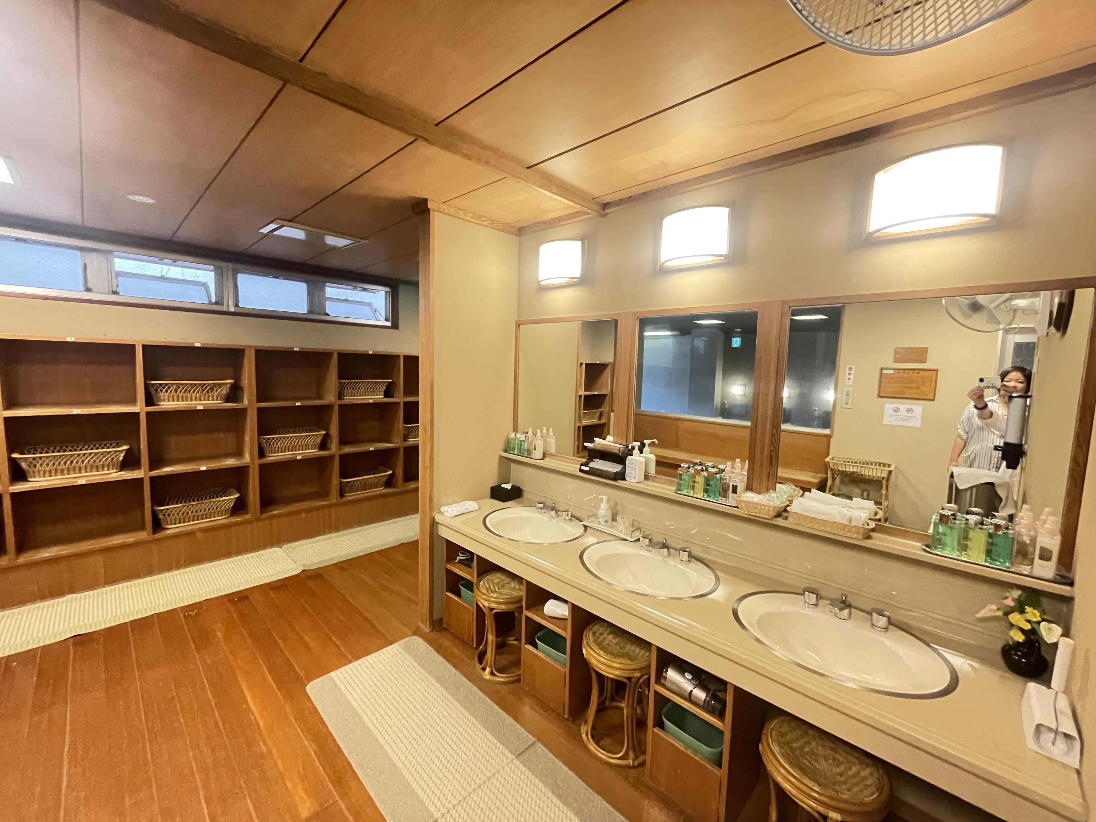 A hotel bathroom with wooden shelves, three sinks, and a large mirror.