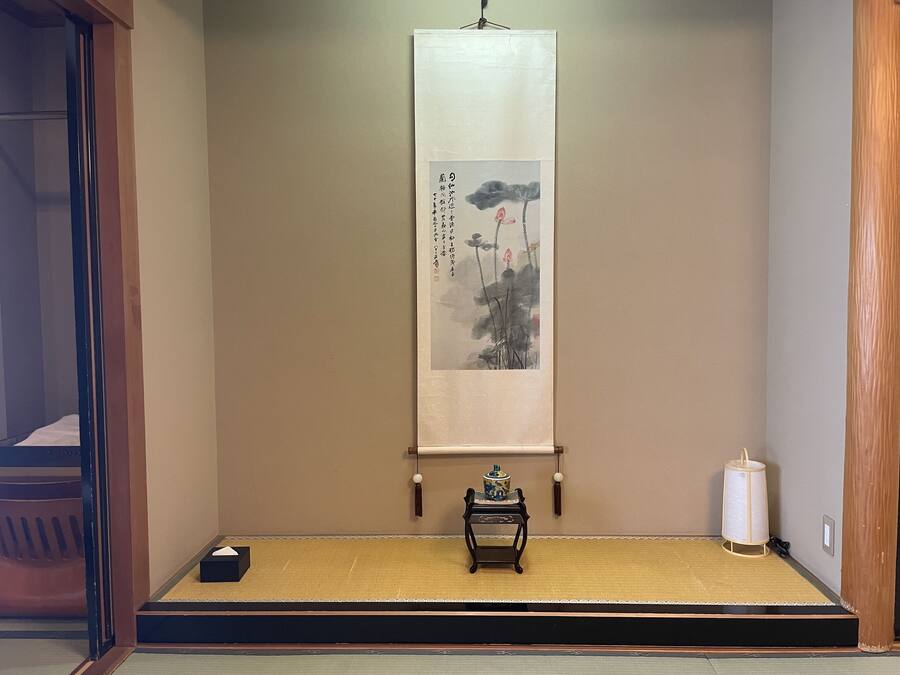 A traditional Japanese room with tatami flooring, a shoji screen, and a hanging scroll with calligraphy.