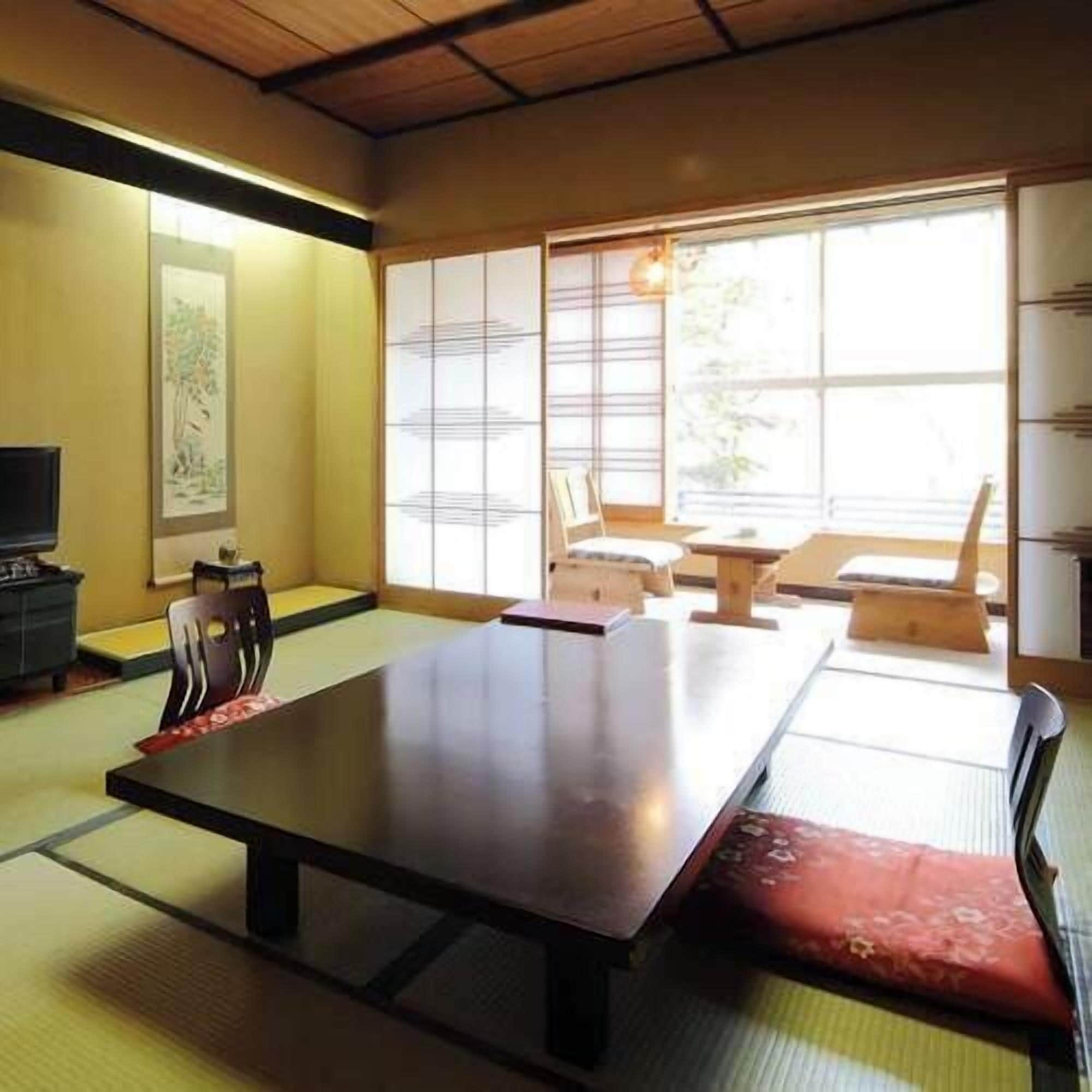 A tatami mat room with a low table, chairs, and a television.