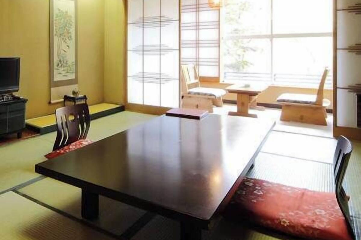A tatami mat room with a low table, chairs, and a television.
