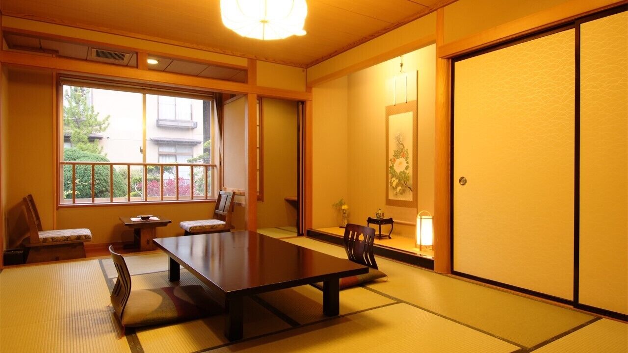 A traditional Japanese room with tatami flooring, a low table, chairs, and sliding doors.