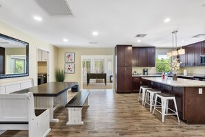 A modern kitchen with wooden flooring, a central island with stools, dark cabinets, and a large mirror. - Vista Villa (Scottsdale)