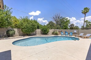 A swimming pool with a curved edge, surrounded by a concrete deck. There are lounge chairs and a small garden area with various plants and trees. - Vista Villa (Scottsdale)
