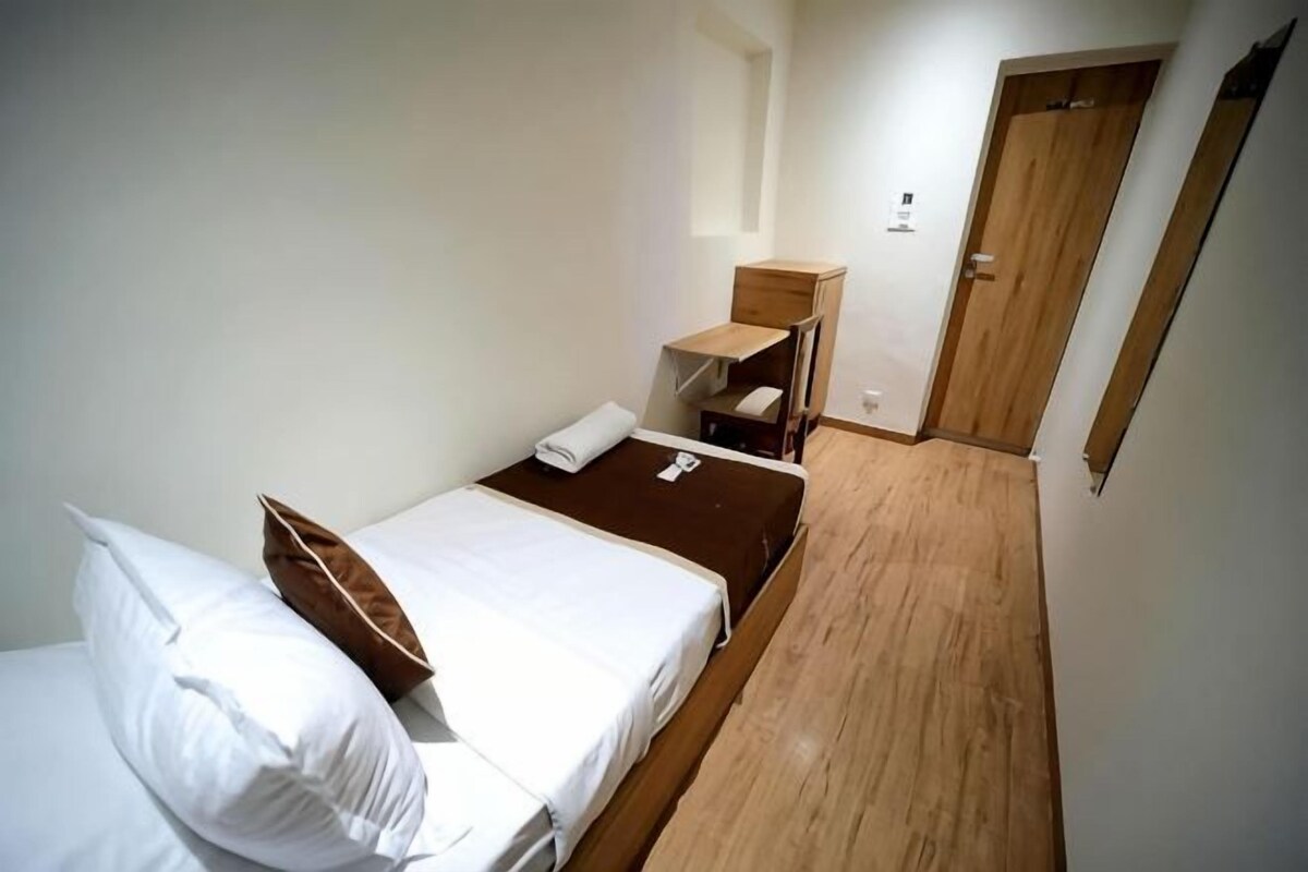 A small, single-bed room with a wooden floor, a bedside table, a chair, and a wardrobe.