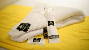 A bed with a yellow sheet, a white towel, and a dental kit. - CABIN STAY AIRPORT-THE HUBZ (Mumbai)