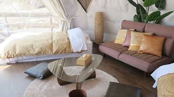 A modern bedroom with a bed, a glass coffee table, a sofa, and a large plant.