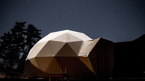 Una tienda en forma de domo geodésico con una mesa y una silla frente a ella, sobre un cielo nocturno estrellado.