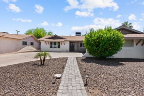 Una proprietà residenziale con vialetto in pietra, una piccola palma e un giardino curato con ghiaia e un albero con fiori arancioni.