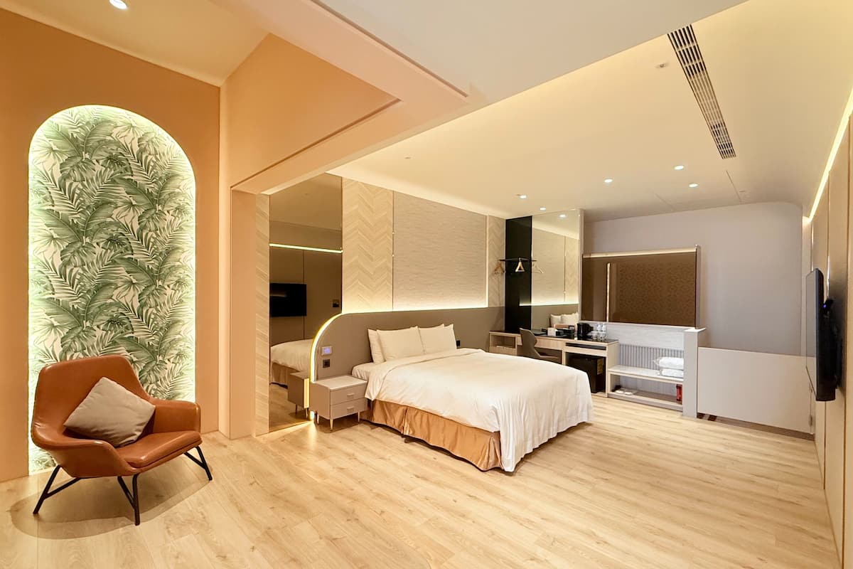 A modern hotel room with a large bed, a desk, a chair, and a mirror.