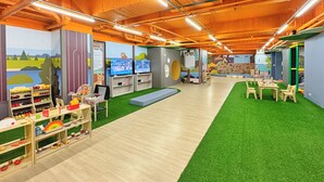 Un espace de jeux pour enfants avec une pelouse artificielle, des tables en bois et des étagères remplies de jouets.