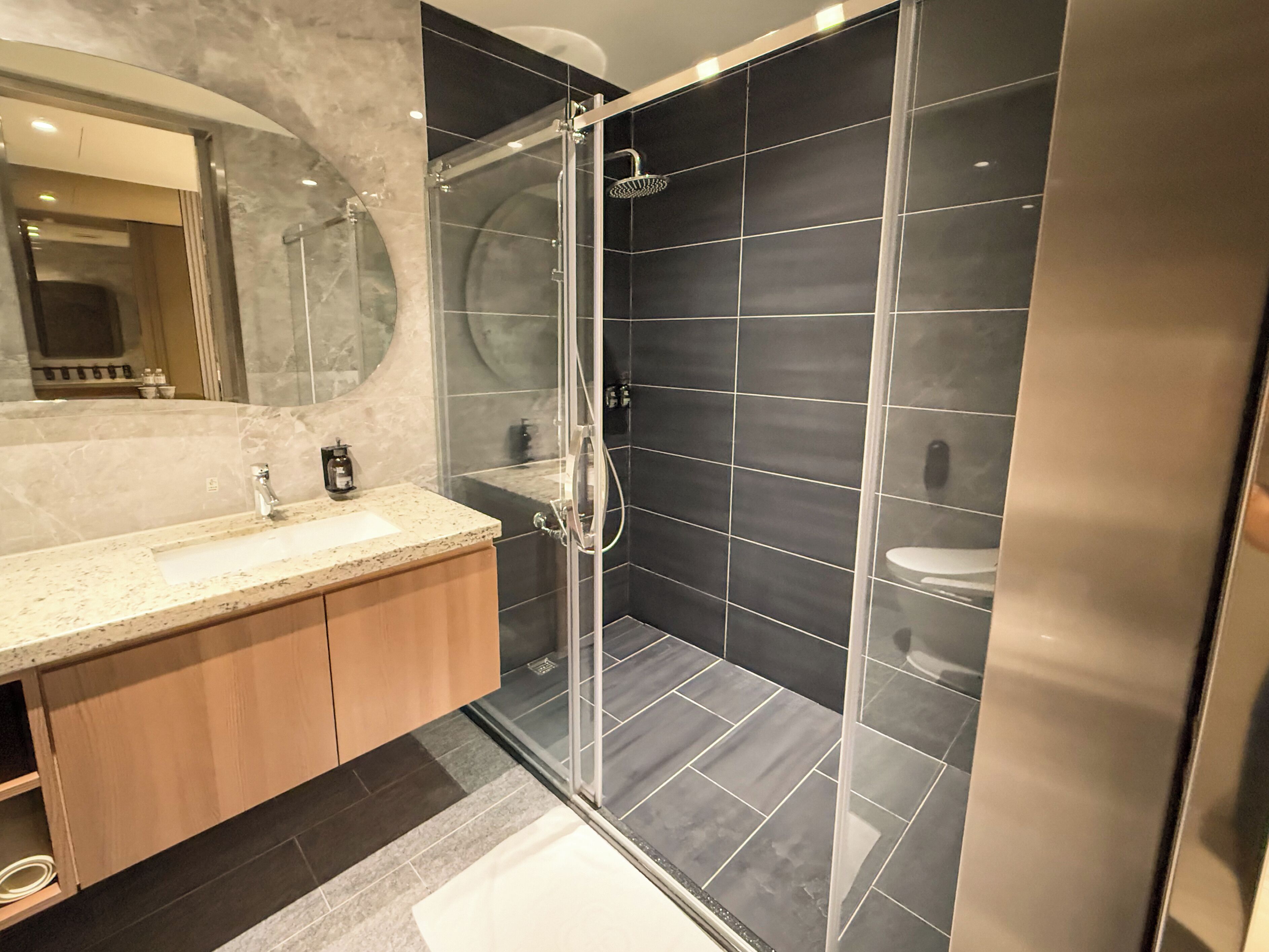 A modern bathroom with a glass-enclosed shower, a marble sink, and dark tiled walls.