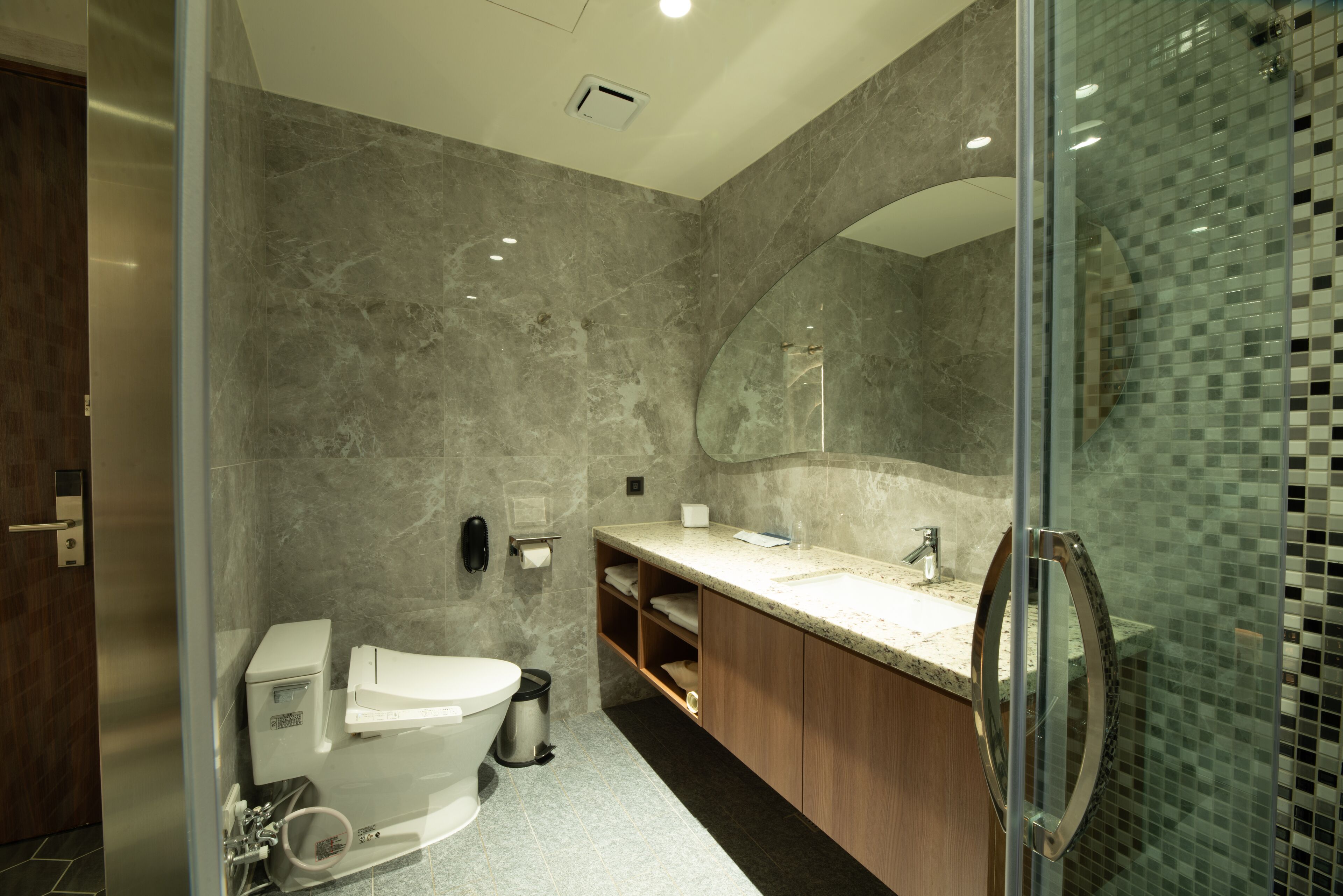 Een moderne badkamer met een douchecabine van glas, een wand betegeld met marmer en een houten wastafelmeubel met een wastafel.