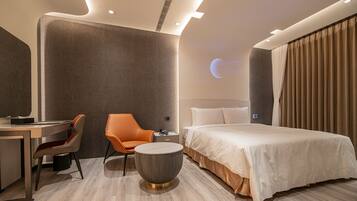 Quarto de hotel moderno com uma cama, uma escrivaninha, uma poltrona laranja e uma mesa de centro redonda.