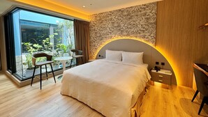Une chambre moderne avec un grand lit, un bureau et une vue sur un jardin, accessible par une porte vitrée.