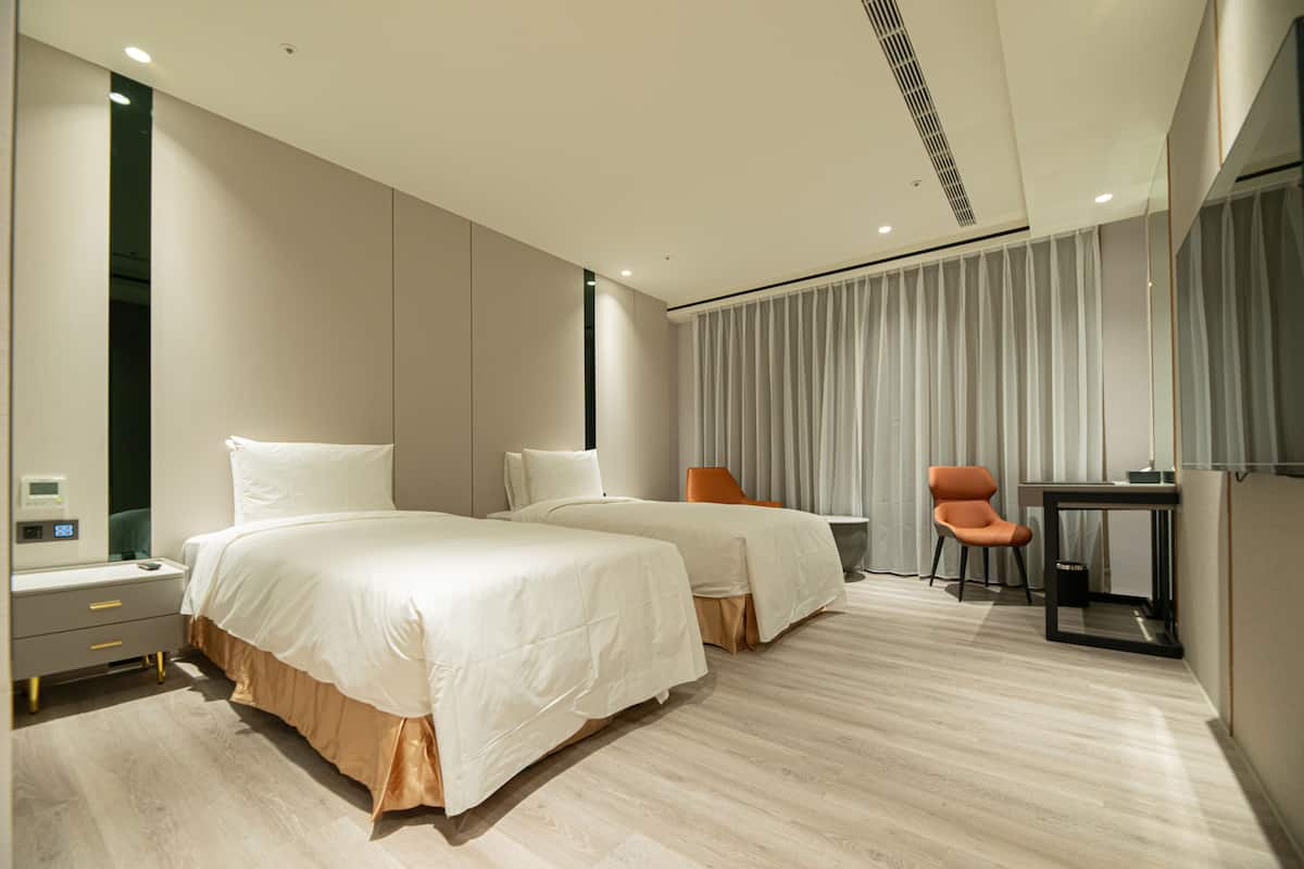A modern hotel room with two beds, a desk, and a chair.