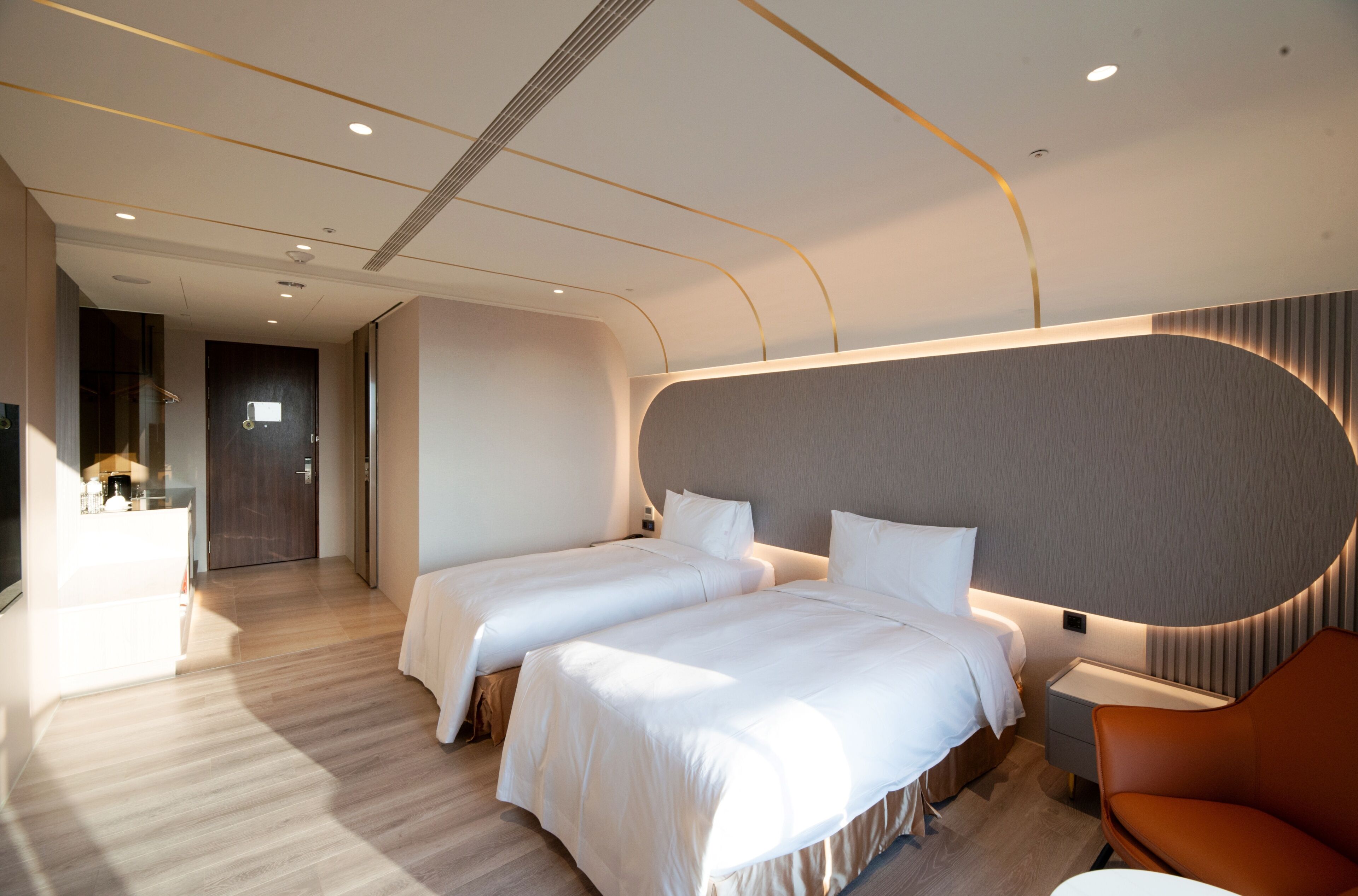 A modern hotel room with two beds, a sitting area, and a bathroom.