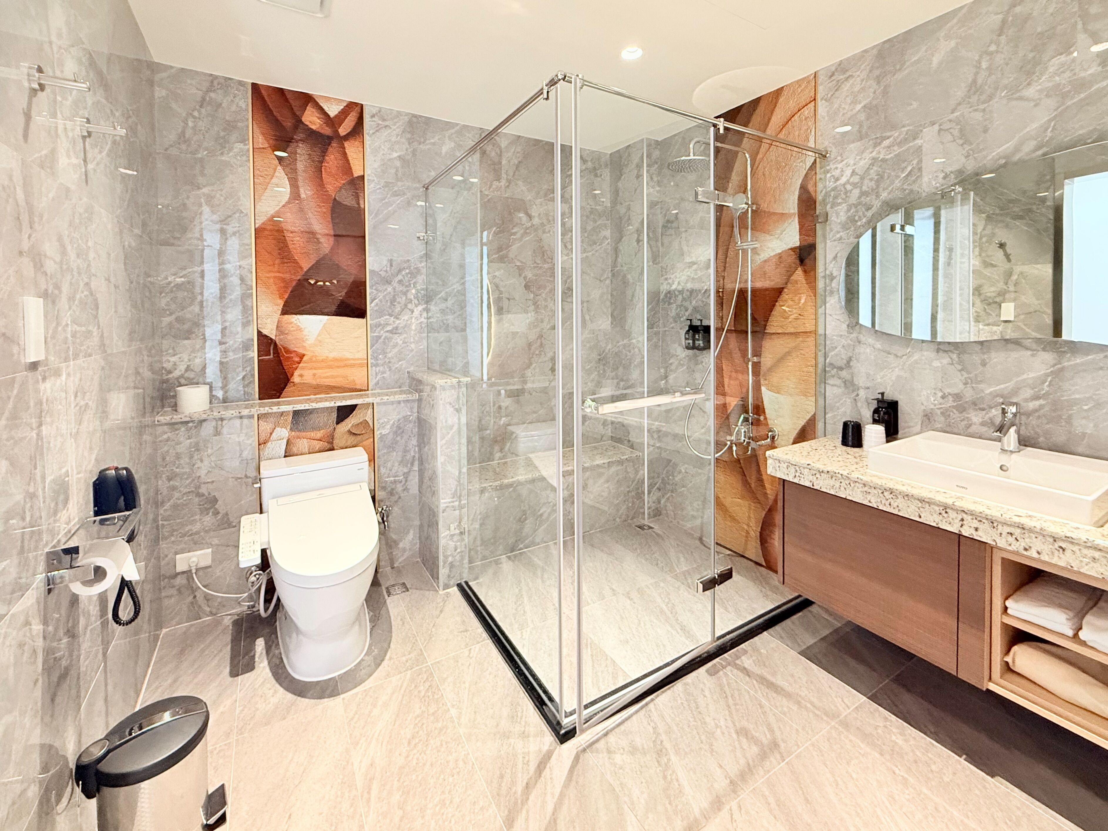 A modern bathroom with a glass-enclosed shower, a white toilet, and a vanity with a sink and mirror.