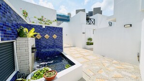 Un espace extérieur moderne agrémenté d’un petit élément décoratif aquatique, de plantes en pot et d’un sol carrelé à motifs.
