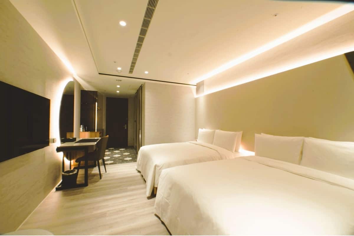 A modern hotel room with two beds, a desk, and a chair.