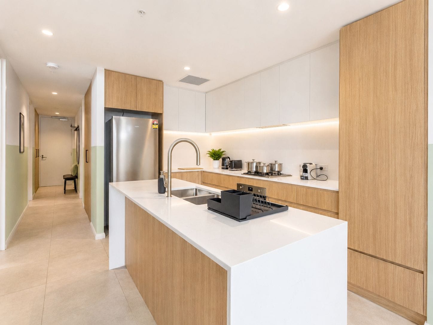 A modern kitchen with a stainless steel refrigerator, a sink, and a countertop with a kettle and pots.
