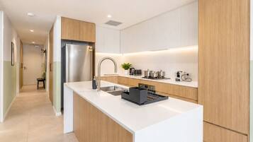 A modern kitchen with a stainless steel refrigerator, a sink, and a countertop with a kettle and pots.