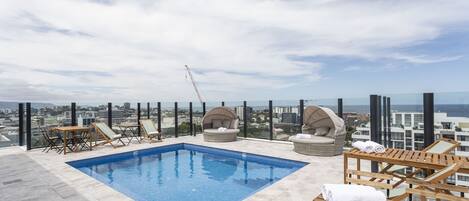 A rooftop pool with lounge chairs and a view of the city.