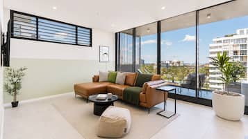 A modern living room with a sectional sofa, a coffee table, and a large window offering a city view.
