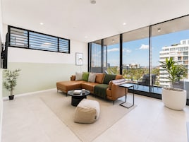 A modern living room with a sectional sofa, a coffee table, and a large window offering a city view.