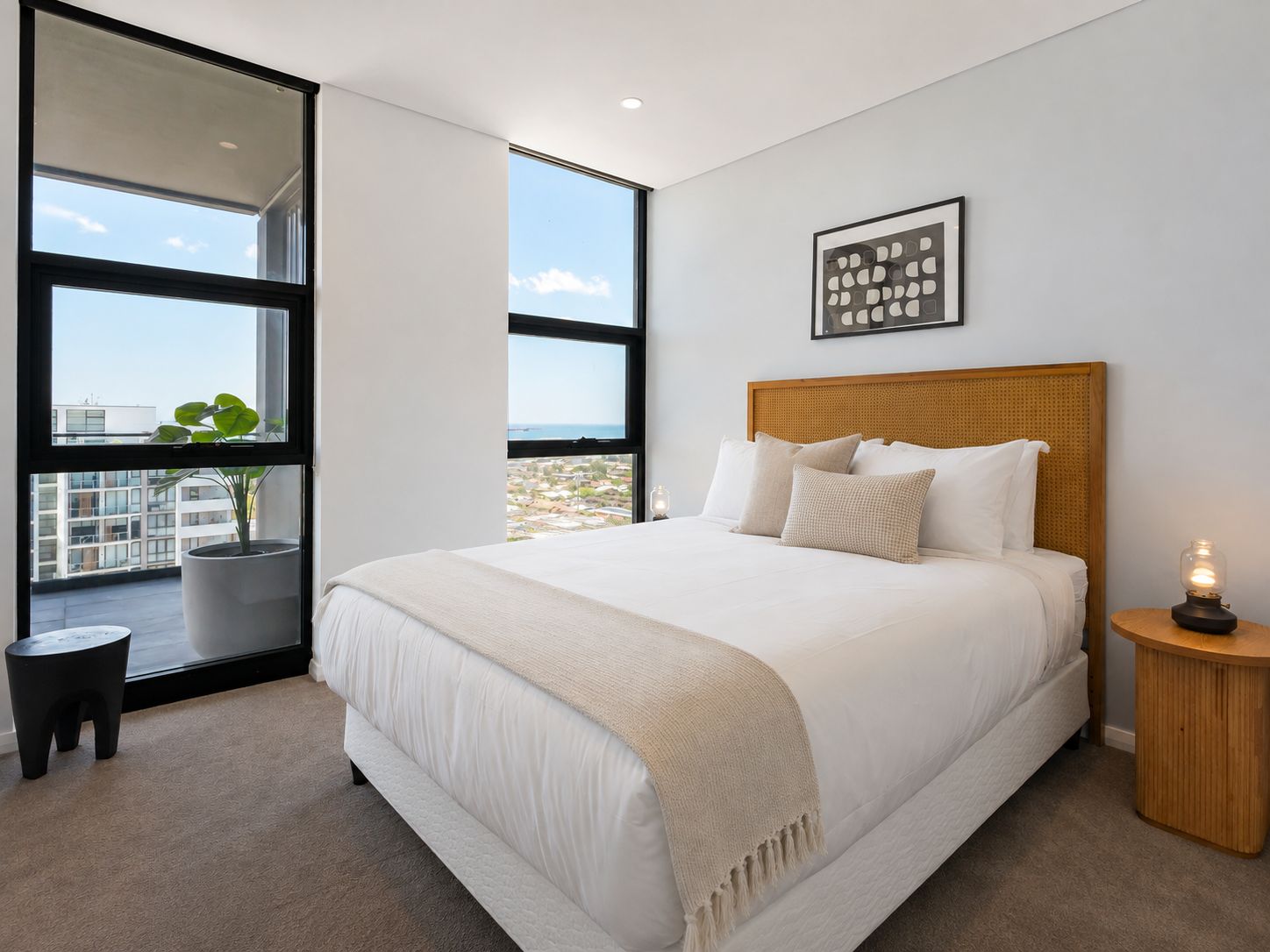 Un dormitorio con una cama grande, una ventana con vistas, una mesita de noche con lámpara y un cuadro enmarcado en la pared.