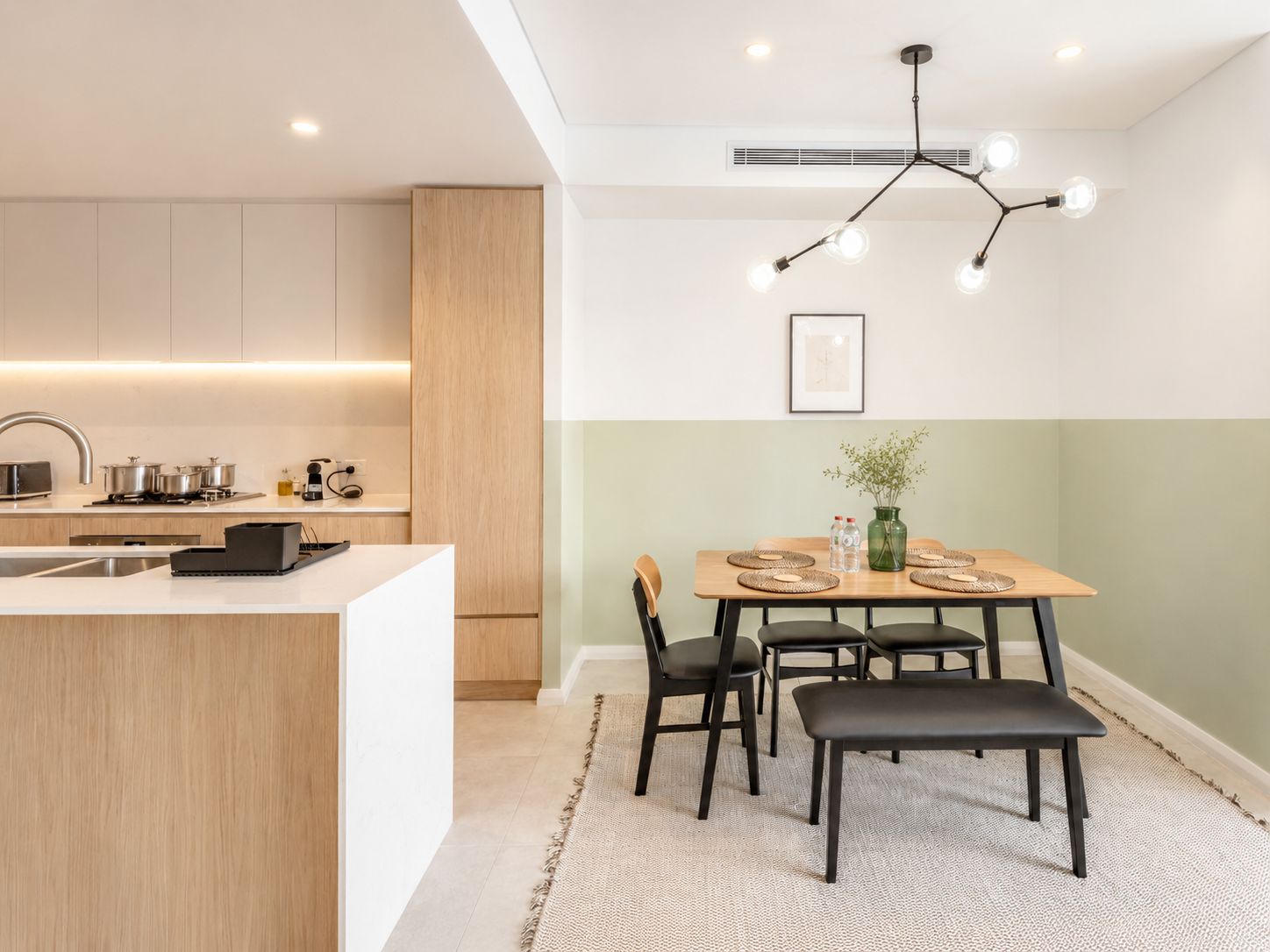 Une cuisine moderne dotée d’un îlot central, d’un coin repas avec une table et des chaises, et d’un luminaire suspendu au plafond.