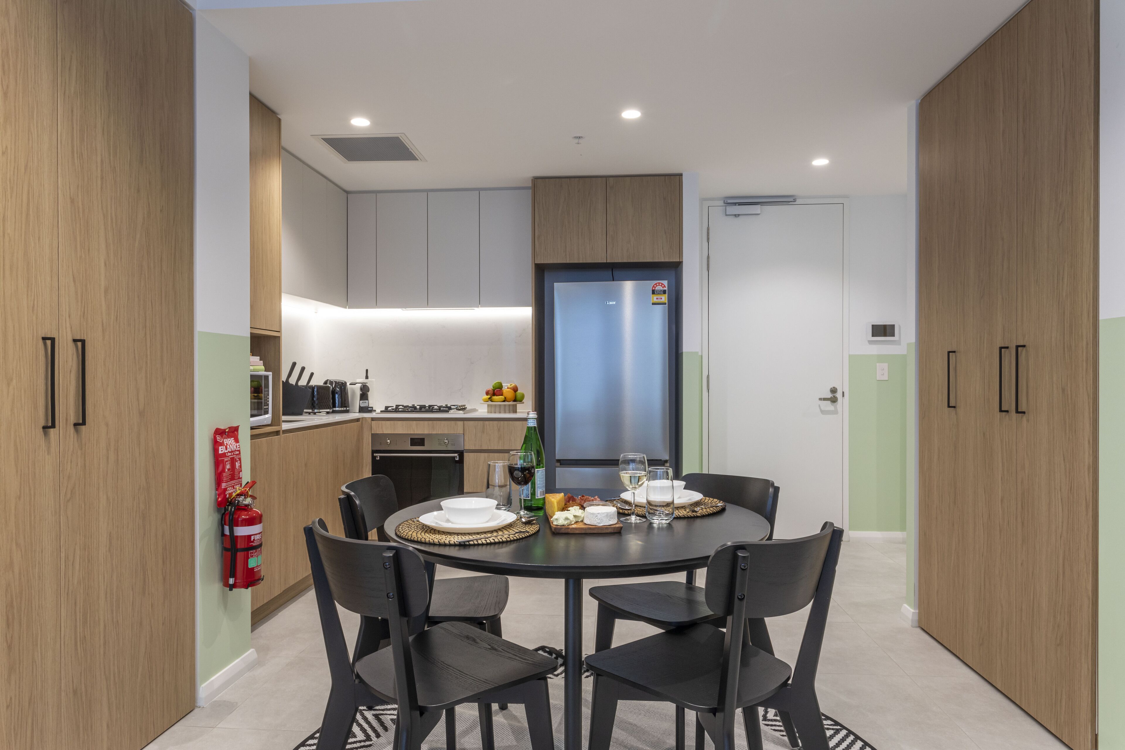 Une cuisine moderne avec un coin repas, comprenant une table ronde avec des chaises, un réfrigérateur et un extincteur fixé au mur.