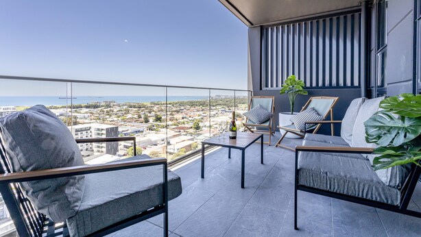 A balcony with a view of the city and the sea, furnished with a sofa, chairs, and a table. - KULA Wollongong (Wollongong)
