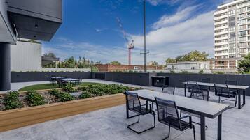 An outdoor patio area with tables and chairs, a small garden, and a view of a construction crane in the background.
