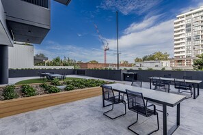 Eine Terrassenanlage im Freien mit Tischen und Stühlen, ein kleiner Garten und im Hintergrund der Blick auf einen Baukran.
