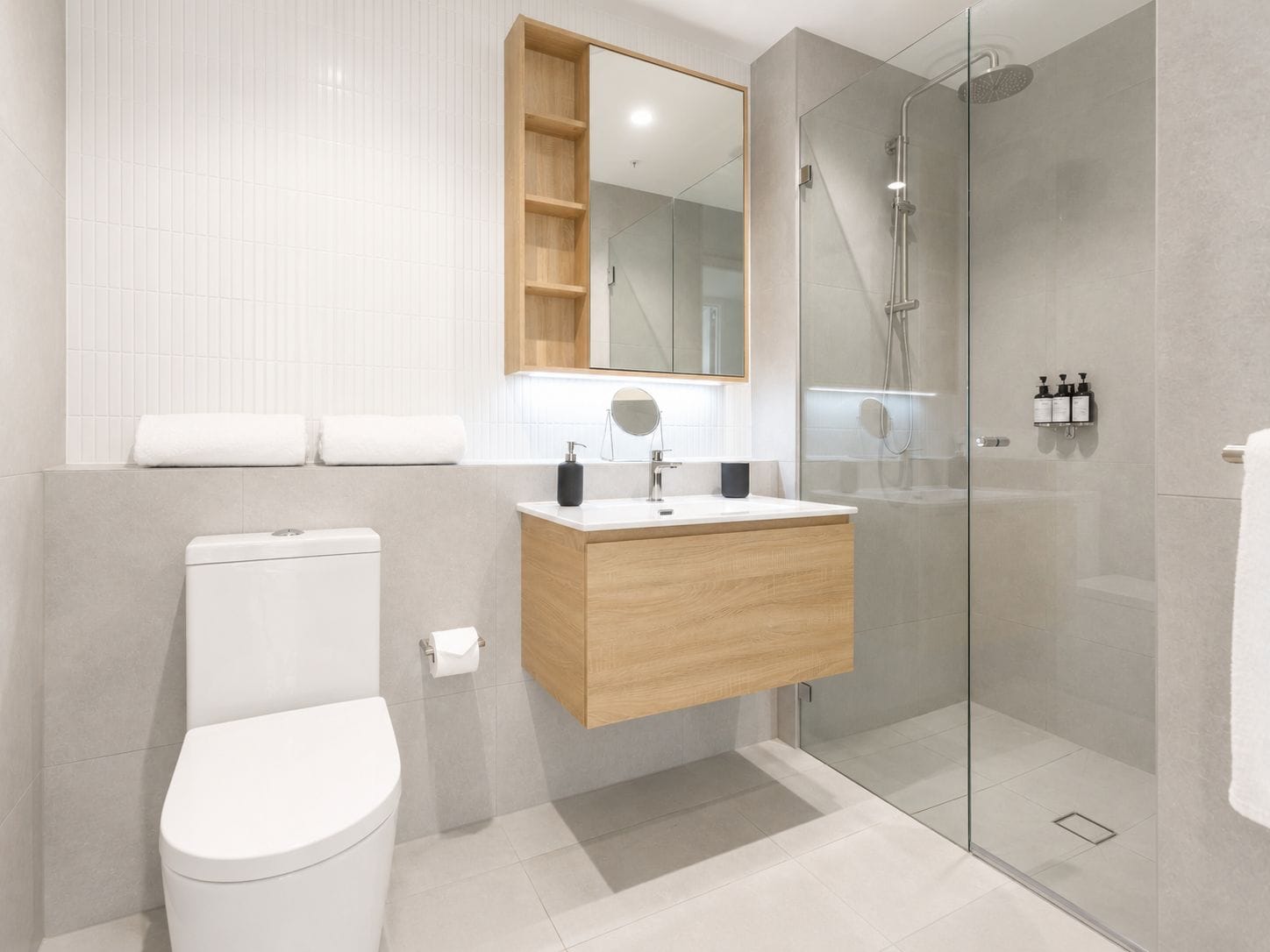 Un baño moderno con inodoro, lavamanos, espejo y ducha con mampara de vidrio.