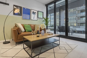 A modern living room with a leather sofa, a wooden coffee table, and a large window offering a view of the outside.