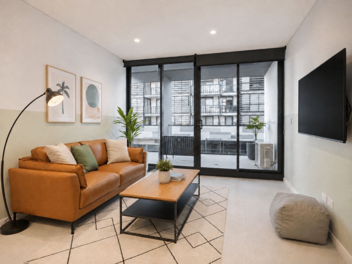A modern living room with a leather sofa, a coffee table, a floor lamp, and a large window offering a view of the cityscape.