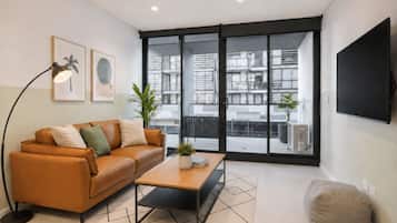 A modern living room with a leather sofa, a coffee table, a floor lamp, and a large window offering a view of the cityscape.