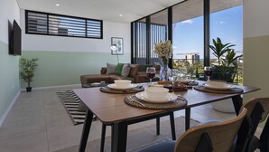 A dining area with a table set for four, a sofa, and a large window with a view. - KULA Wollongong (Wollongong)