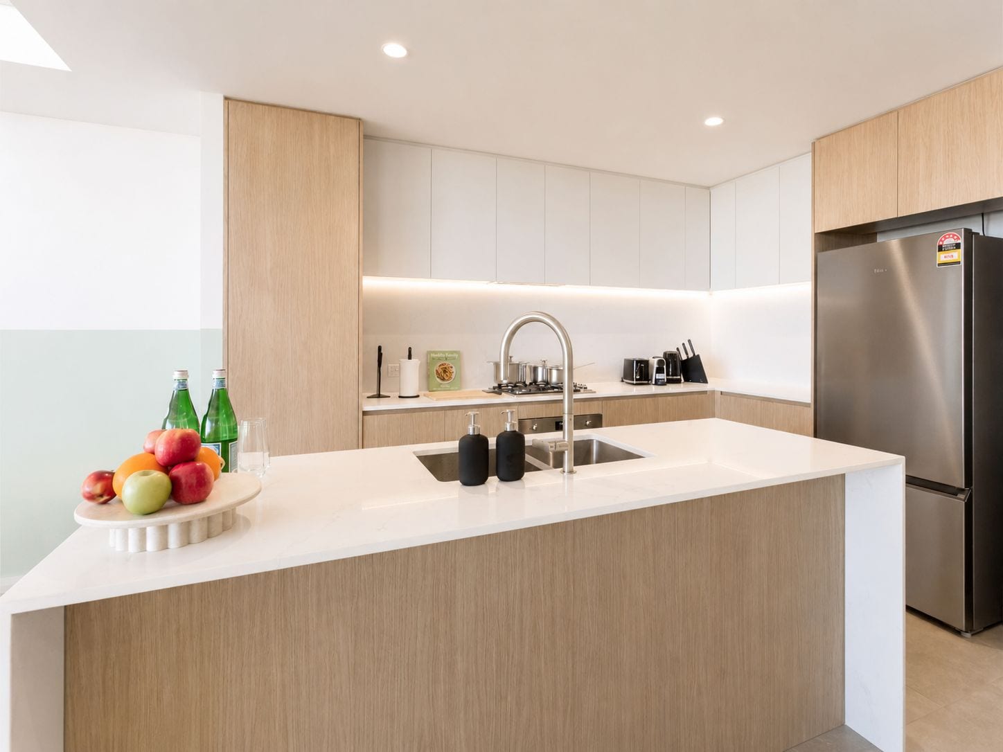 Une cuisine moderne dotée d’un îlot central, d’appareils électroménagers en acier inoxydable et d’un panier à fruits.